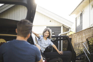 Portrait of mother, father and two daughters standing by car at electric vehicle charging station - MASF26178