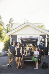 Portrait of mother, father and two daughters standing by car at electric vehicle charging station - MASF26183