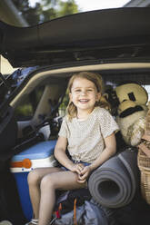 Porträt einer Mutter, eines Vaters und zweier Töchter, die neben einem Auto an einer Ladestation für Elektrofahrzeuge stehen - MASF26185