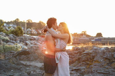 Junges Paar, das sich küsst, während es bei Sonnenuntergang auf einem Felsen am Meer steht - MASF26201
