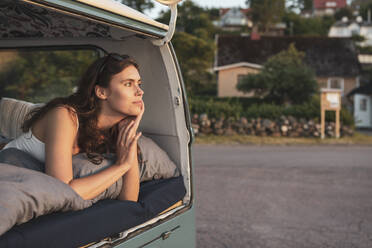 Junge Frau beim Nachdenken im Liegen in einem Van während einer Autoreise - MASF26205