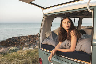 Woman looking away while lying in camping van during sunset - MASF26206