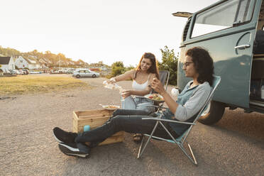 Young couple having food outside camping van in evening - MASF26208