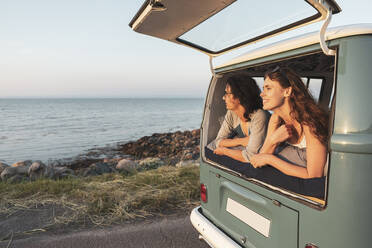 Female and male friends looking at sea from camping van during road trip - MASF26211