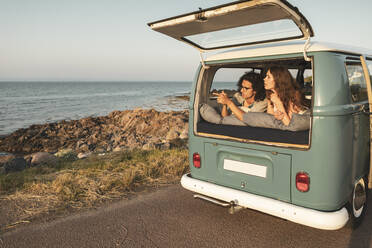 Young couple looking at sea while lying down in van - MASF26220