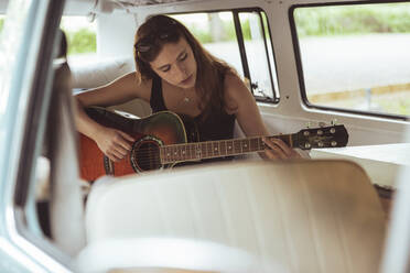 Junge Frau spielt Gitarre, während sie während einer Autoreise im Van sitzt - MASF26243