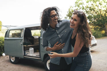 Happy young couple standing outside camping van - MASF26265