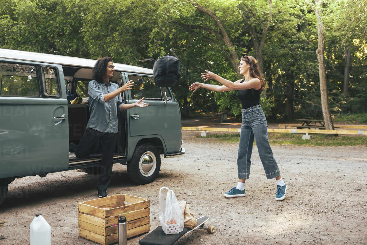 Male and female friends throwing backpack while standing outside camping  van stock photo