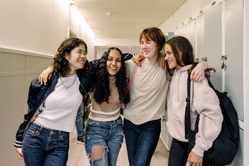 Lächelnde Freundinnen stehen zusammen im Korridor der Schule - MASF26267