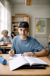 Portrait of teenage boy drawing on book in classroom - MASF26322