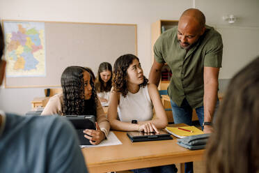 Männlicher Lehrer unterrichtet Teenager-Mädchen über ein digitales Tablet am Schreibtisch im Klassenzimmer - MASF26329