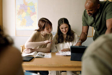 Male professor teaching teenage girls at desk in high school classroom - MASF26330