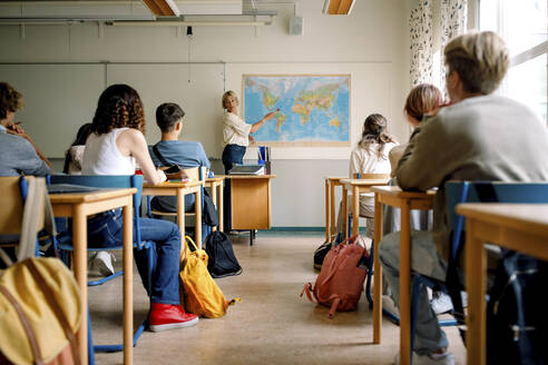 Lehrerin unterrichtet Mädchen und Jungen im Klassenzimmer über Landkarten - MASF26343