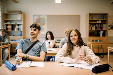 Lächelnde Gymnasiasten mit Buch und Stift im beleuchteten Klassenzimmer - MASF26345