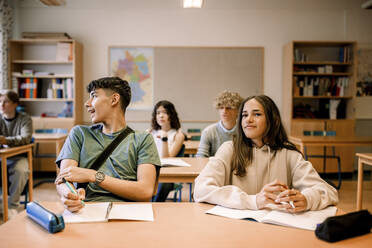 Jungen und Mädchen sitzen mit Buch auf dem Schreibtisch im Klassenzimmer - MASF26349