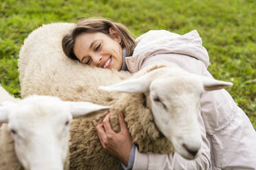 Smiling mid adult woman embracing sheep in farm - DIGF16561