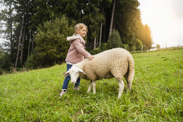 Smiling cute girl standing with sheep in green farm - DIGF16562