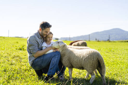 Lächelnder Vater und Tochter streicheln Schafe auf einem Bauernhof - DIGF16570