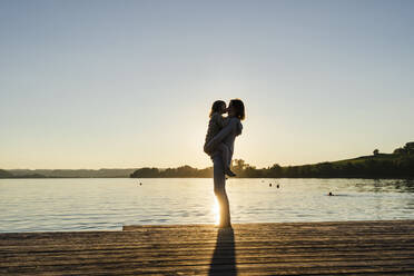 Mutter küsst Tochter, während sie bei Sonnenuntergang auf dem Steg steht - DIGF16573