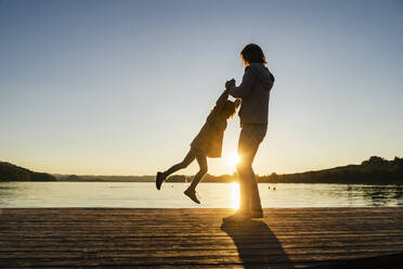 Mother spinning daughter over pier during sunset - DIGF16577