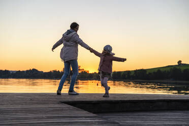 Mother and daughter dancing on pier during sunset - DIGF16579