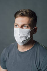 Young man looking away while wearing protective face mask - MEUF04300