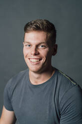 Smiling young man in gray t-shirt at studio - MEUF04301