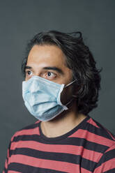 Mid adult man looking away while wearing protective face mask in studio - MEUF04308