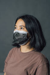 Junge Frau, die wegschaut, während sie eine Gesichtsschutzmaske trägt - MEUF04330