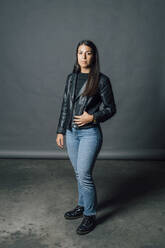 Young confident woman in leather jacket standing in studio - MEUF04342