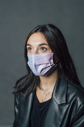 Junge Frau mit schwarzem Haar und Gesichtsschutzmaske in einem Studio während einer Pandemie - MEUF04355