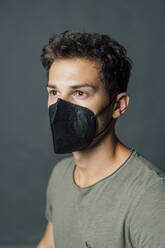 Young man looking away while wearing protective face mask during pandemic - MEUF04369