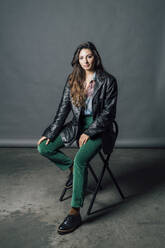 Confident woman in leather jacket sitting on chair - MEUF04371