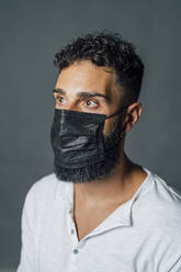 Young man looking away while wearing protective face mask in studio - MEUF04385