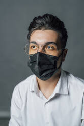 Young man wearing protective face mask and eyeglasses in studio - MEUF04390