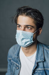 Junger Mann mit Schutzmaske während einer Pandemie - MEUF04412