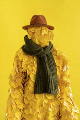 Frau mit Blattkostüm, Schal und Hut vor gelbem Hintergrund - VPIF05041