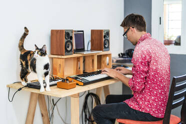 Male musician playing piano while sitting on chair - DLTSF02234