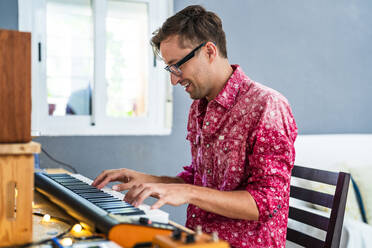 Lächelnder Mann mit Brille spielt zu Hause Klavier - DLTSF02235
