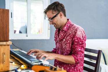 Smiling man with eyeglasses playing piano at home - DLTSF02235