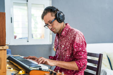 Male musician wearing headphones while playing piano at home - DLTSF02236