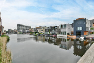 Zeitgenössische Hausfassaden spiegeln sich in gekräuselten Fluss unter Brücke und bewölktem Himmel in Amsterdam Holland - ADSF31020