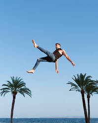 From below side view of energetic sportsman in trendy wear performing trick against blue sky in sunlight - ADSF31026