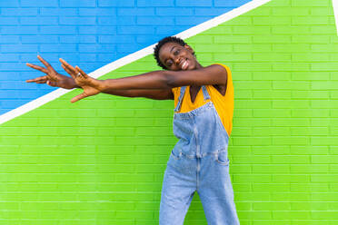Glückliche junge Afroamerikanerin, die lächelnd auf einer bunten, hellen Wand steht - ADSF31038