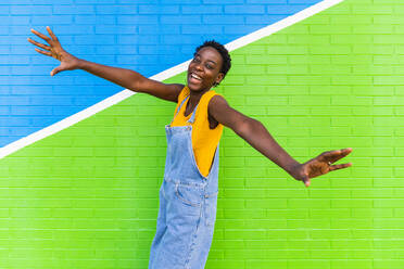 Seitenansicht einer glücklichen afroamerikanischen Frau, die lächelnd über den Boden in der Nähe einer hellen Wand springt - ADSF31040