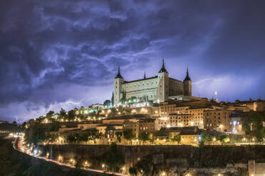 Stadtbild mit gealtertem berühmten Schloss Alcazar von Toledo in Spanien unter bewölktem Himmel in der Nacht während eines Gewitters platziert - ADSF31083