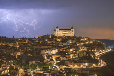 Stadtbild mit gealtertem berühmten Schloss Alcazar von Toledo in Spanien unter bewölktem Himmel in der Nacht während eines Gewitters platziert - ADSF31085