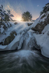 Langzeitbelichtung eines schnellen Wasserfalls, der durch verschneites Gelände im Nationalpark Sierra de Guadarrama fließt - ADSF31091