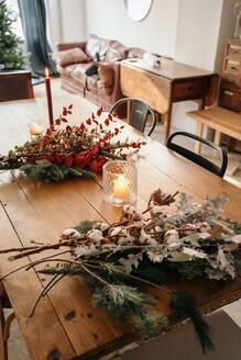 Von oben festlicher Weihnachtsstrauß mit Baumwoll-, Tannen- und Eukalyptuszweigen und leuchtend roten Zweigen mit Beeren auf einem Holztisch mit Kerzen im Zimmer - ADSF31100