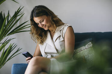 Smiling mid adult woman using smart phone in living room - ABZF03606